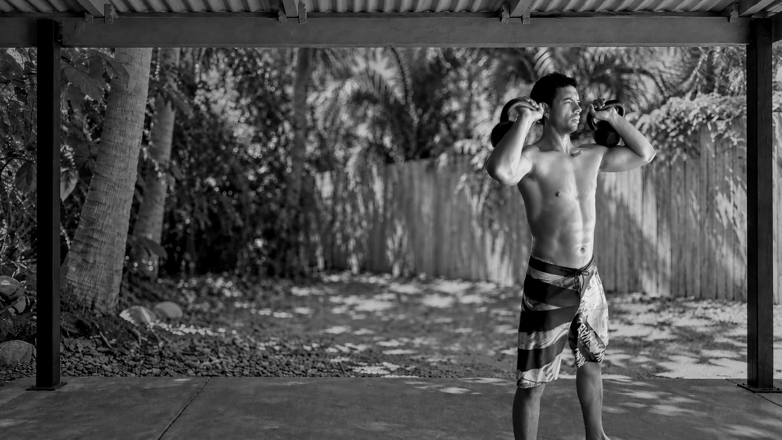 Bruno Bardalez si allena con due kettlebell sotto una tettoia, in un cortile in Australia